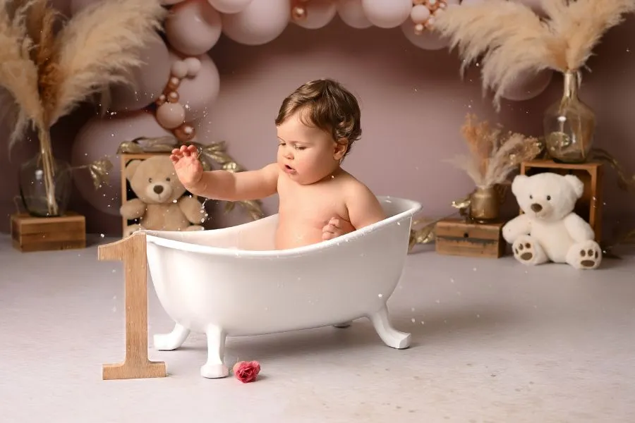 Portrait artistique d'anniversaire d'un bébé dans une petite baignoire qui joue avec un 1 en bois, réalisé dans le studio de Ael Photos à Pont de Buis dans le Finistère