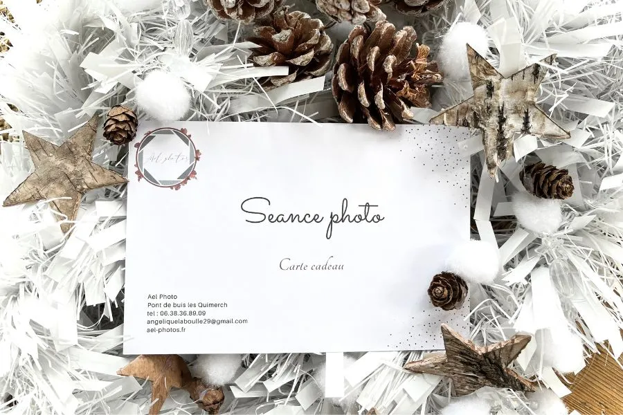 Carte cadeau pour une séance photo avec Ael Photos à Pont de Buis, posée sur un fond de guirlandes blanches, pommes de pin et étoiles en bois