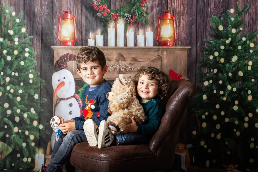 Deux enfants posent dans un décor de Noël cosy au studio AEL Photos, idéal pour les cartes de fin d’année.