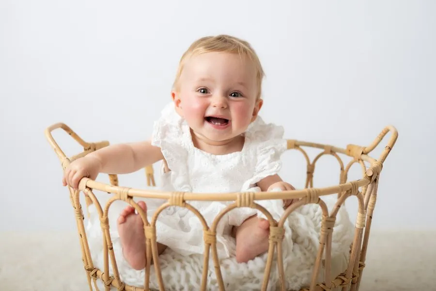 Portrait studio d'un bébé souriant assis dans un panier en osier, par Ael Photos dans son studio à Pont de Buis dans le Finistère