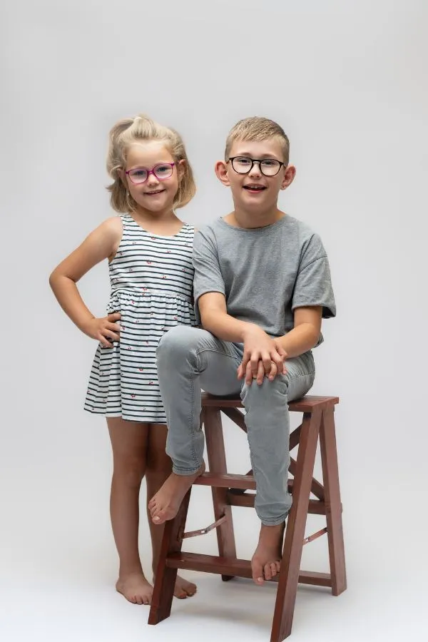 Portrait studio par Ael Photos, deux enfants frère et soeur souriants qui posent l'un assis sur un tabouret et l'autre debout à côté