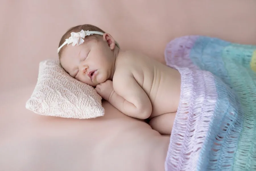 Nouveau-né endormi sur un coussin avec couverture pastel photographié en studio en Bretagne