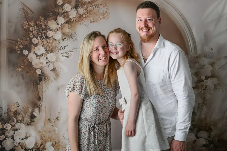Portrait de famille de parents avec leur fillette, mère et fille joue contre joue, tous trois souriants, au studio AEL Photos au Faou en Bretagne