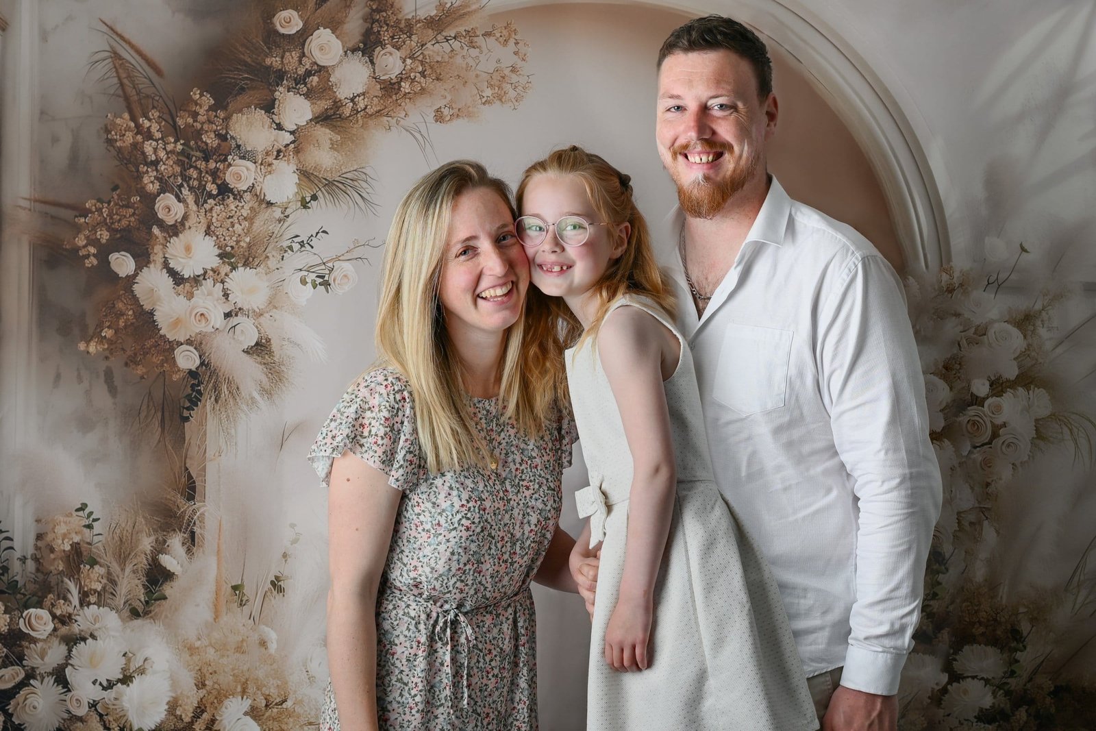 Portrait de famille de parents avec leur fillette, mère et fille joue contre joue, tous trois souriants, au studio AEL Photos au Faou en Bretagne
