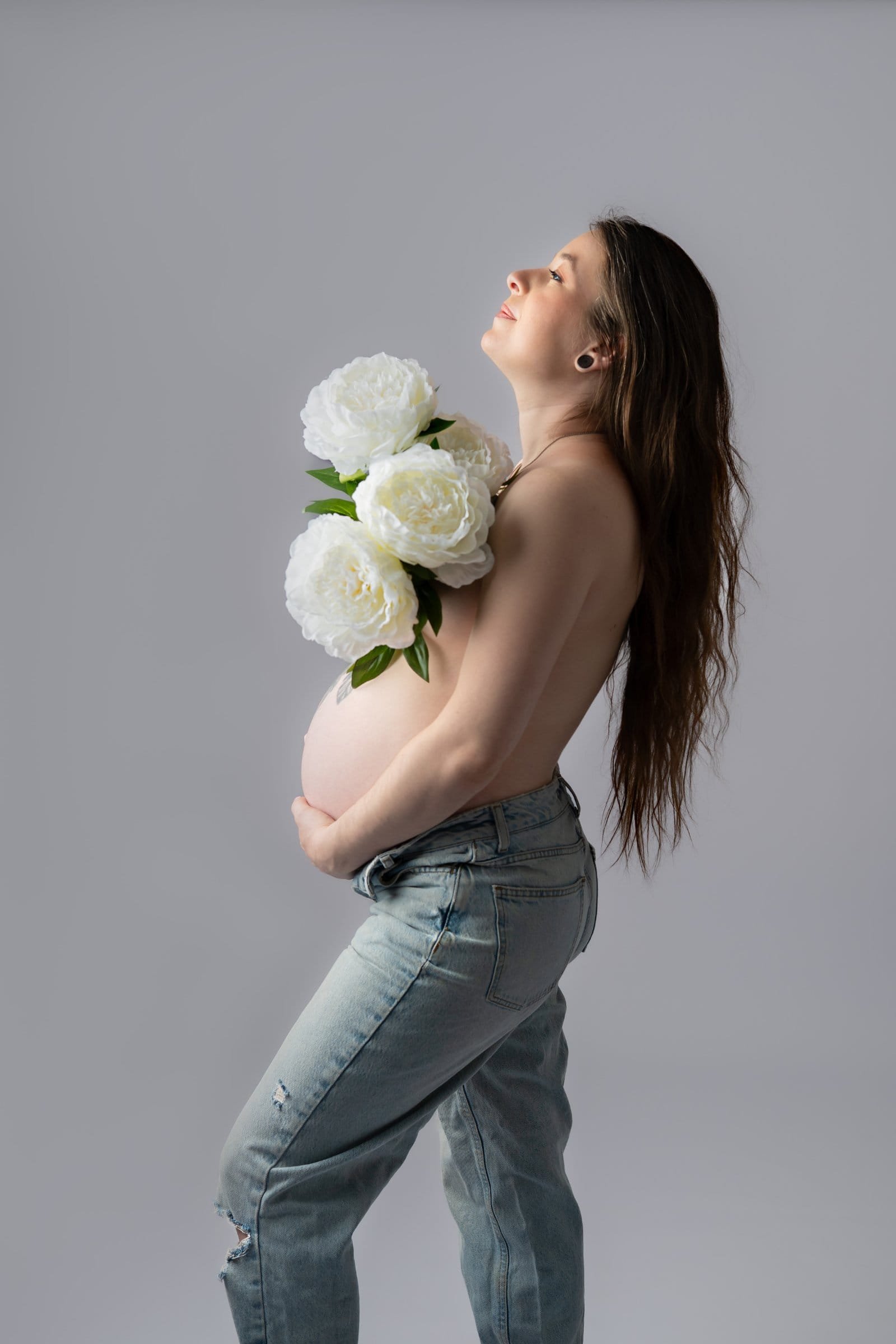 Portrait plein de tendresse d’une future maman tenant des fleurs blanches posées sur son ventre, séance maternité en studio au Faou, entre Brest et Châteaulin.